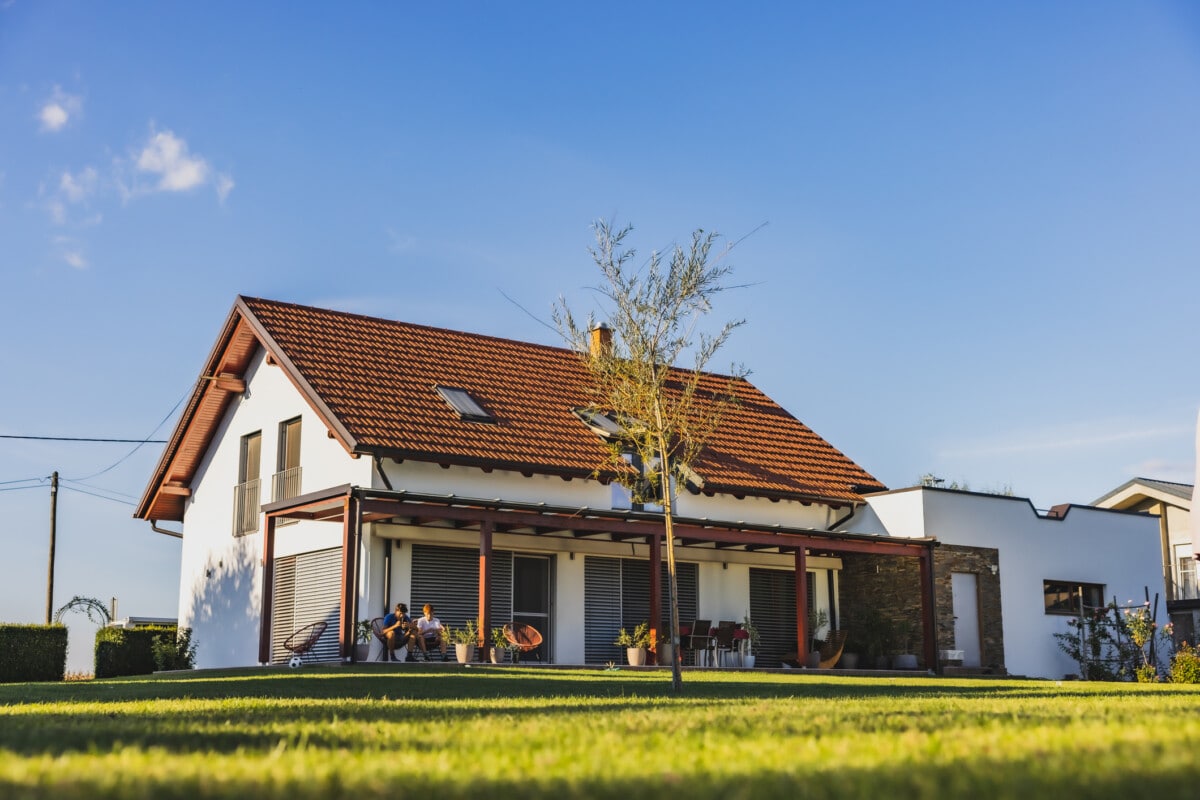 Maison moderne avec terrasse à la campagne, deux garçons assis sur des chaises sur la terrasse et utilisant le téléphone, ciel clair en arrière-plan