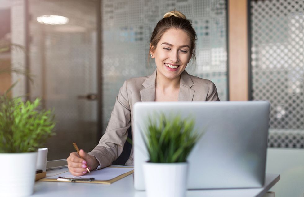 Heureuse jeune femme d'affaires sur un ordinateur portable se préparant à travailler le premier jour dans un nouveau bureau