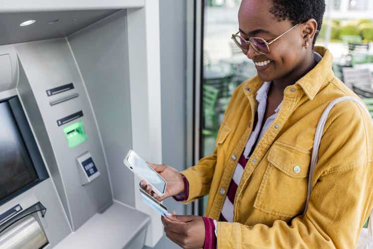 Une femme afro-américaine retire de l’argent à un guichet automatique extérieur