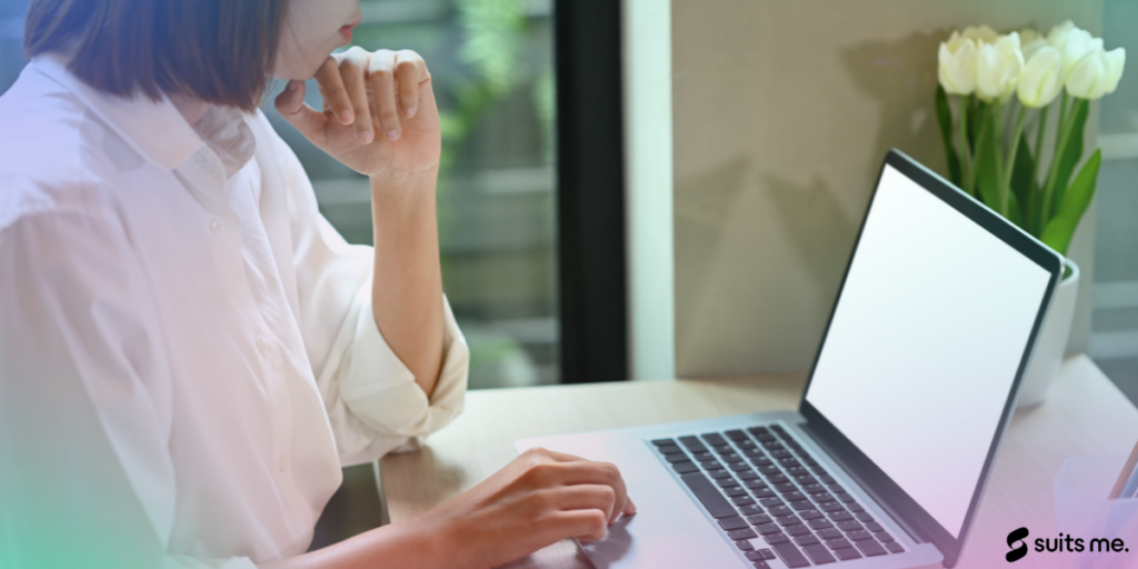 Une femme assise devant son ordinateur portable ouvrant un compte bancaire en ligne sur un bureau avec des fleurs et une fenêtre en arrière-plan.  Brillance dégradée avec logo Suits Me sur le dessus.