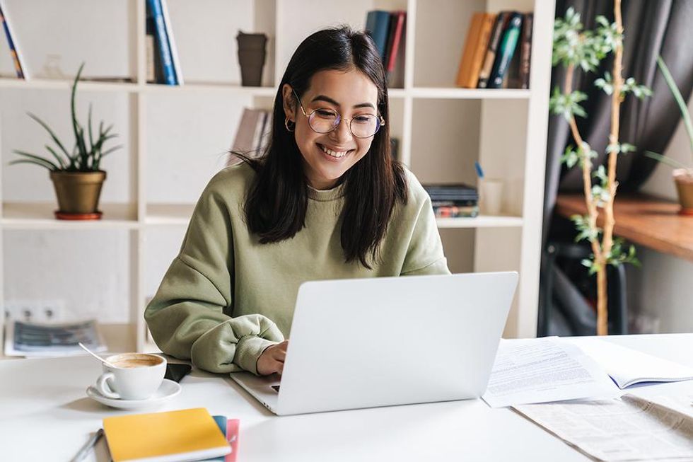 Une jeune femme heureuse sur son ordinateur portable écrit pour un blog tout en cherchant du travail