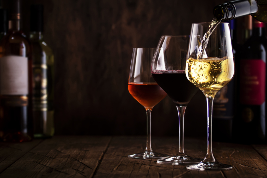 Dégustation de vins.  Vin blanc versé dans un verre sur fond avec sélection de vins rouges, blancs et rosés dans des verres et des bouteilles