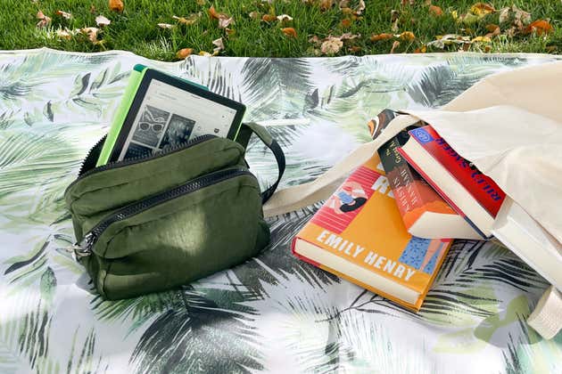 Un sac banane avec un Kindle à l'intérieur à côté d'un sac de livres sur une couverture de pique-nique.